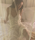 Woman wearing a white crochet dress sitting on a bed.