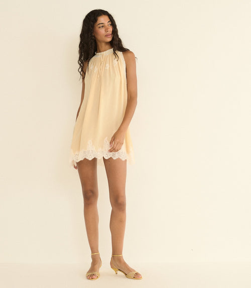 Woman wearing a light beige dress with lace trim on a plain background