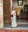 Woman in a white crochet dress standing in an ornate room with decorative elements.