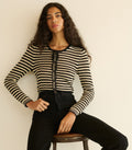 Woman wearing a black and white striped cardigan sitting on a stool against a plain background