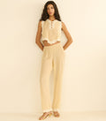 Woman wearing a beige sleeveless top and pants against a beige background