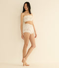 Woman wearing a white crop top and shorts set on a beige background