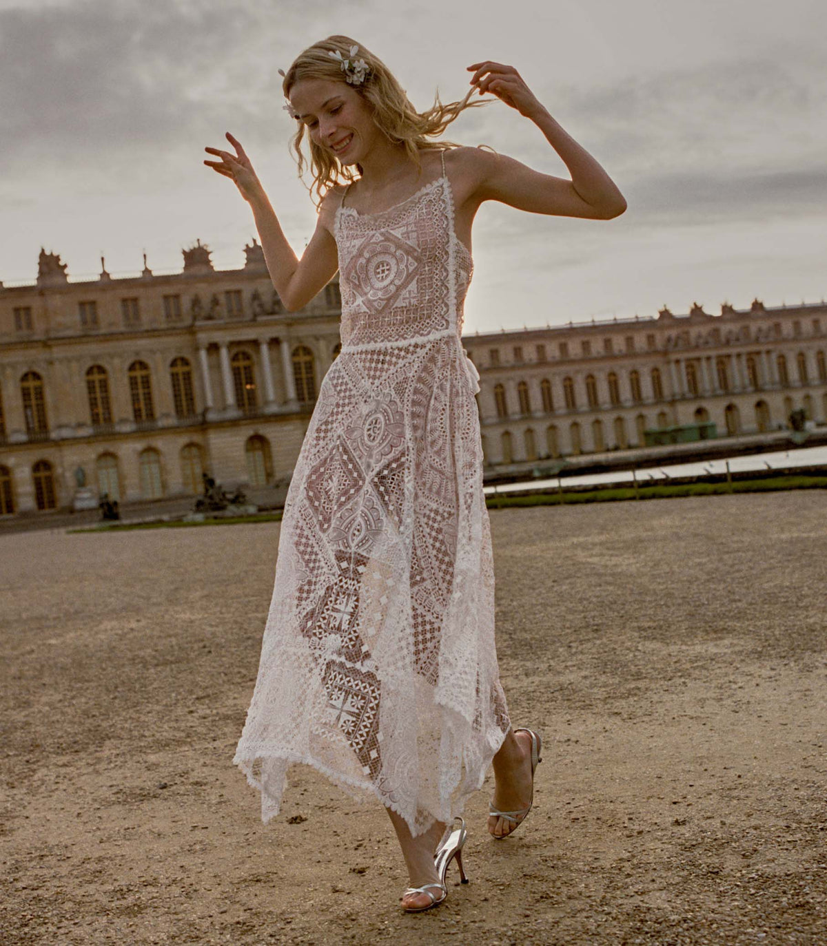 Woman wearing a white crochet dress standing in front of old buildings
