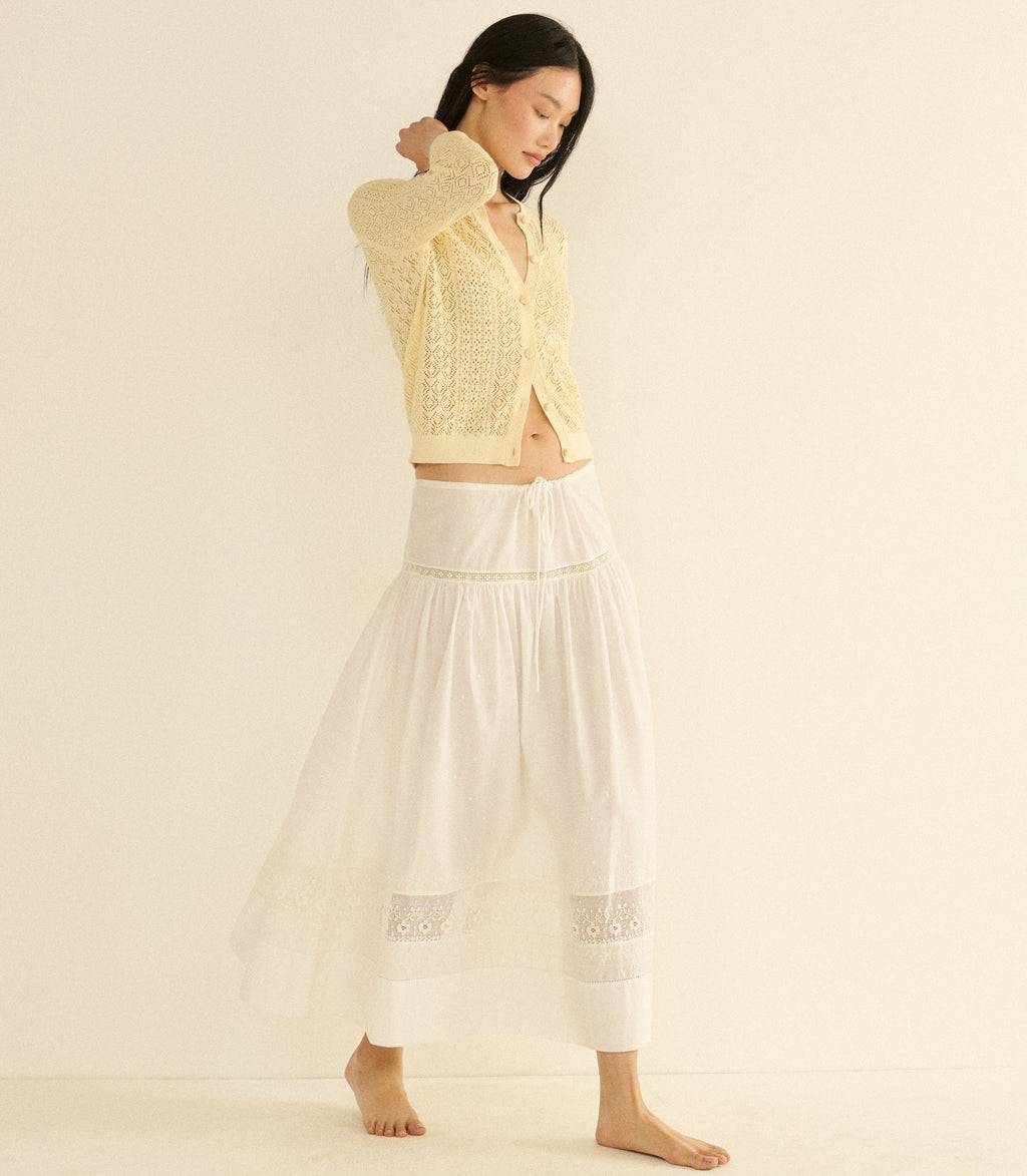 Woman wearing a yellow textured cardigan and white skirt on a beige background