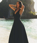 Woman in a black dress standing by a body of water with cliffs in the background