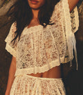 Person wearing a white lace top and skirt against a blurred natural background